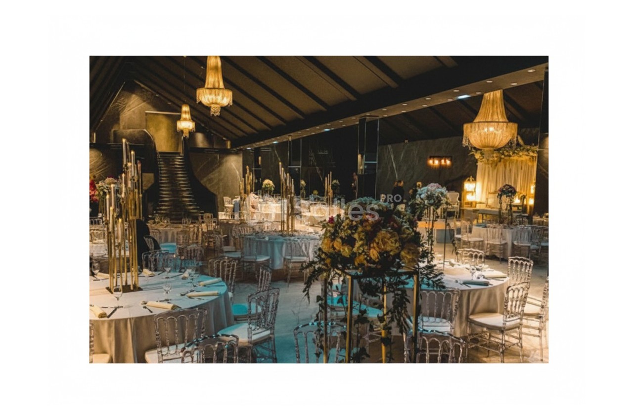 Salle de réception élégante avec tables dressées, chaises transparentes et lustres suspendus dans une ambiance tamisée.