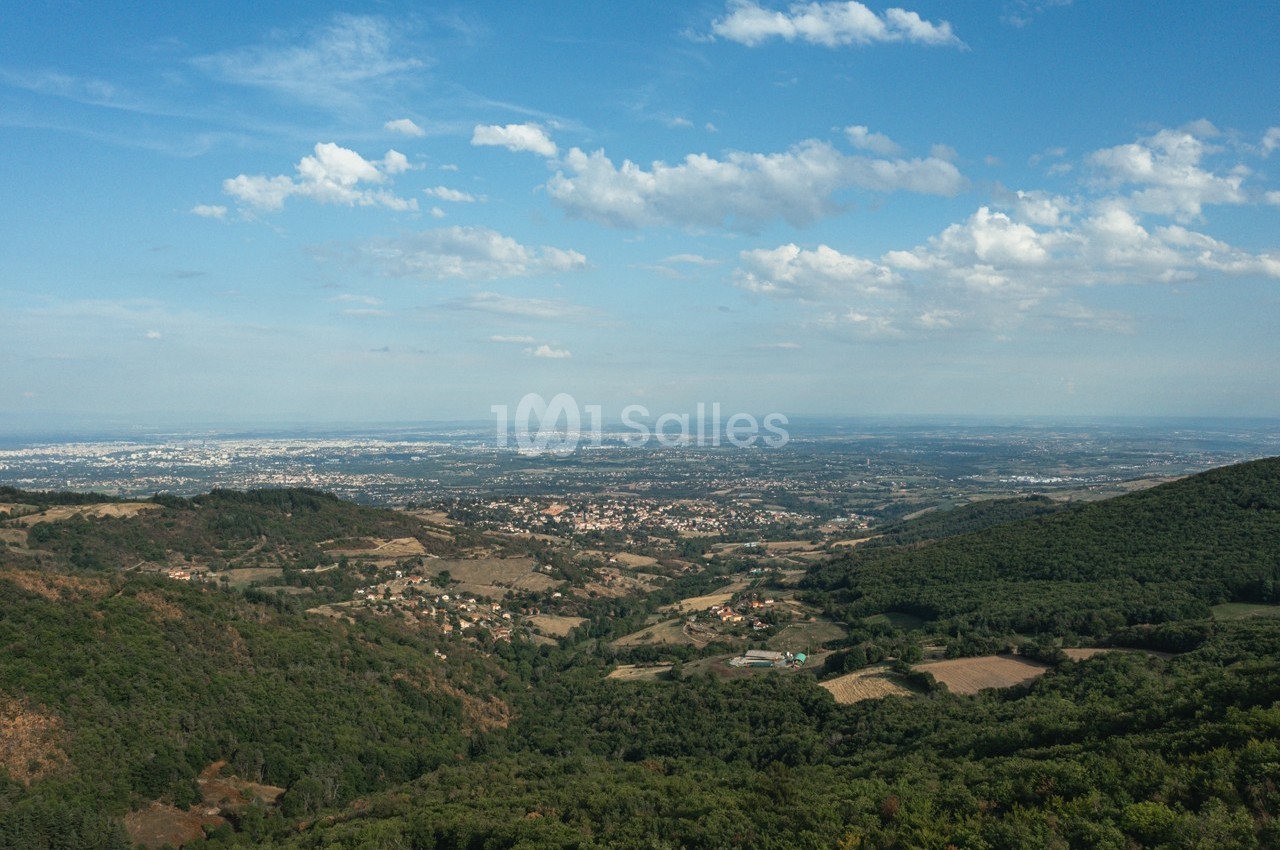 Vue aérienne d'une vallée verdoyante avec des collines, des villages et un ciel partiellement nuageux à l'horizon.