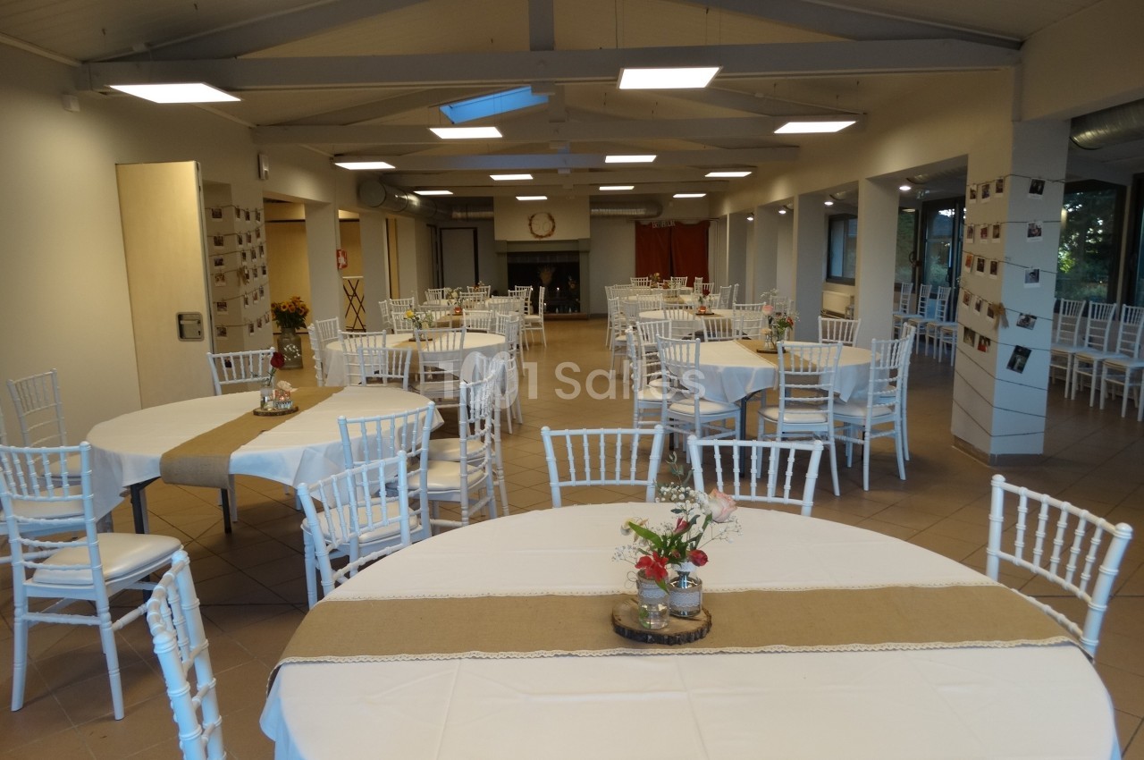 Salle de réception lumineuse avec des tables rondes et rectangulaires décorées de nappes blanches et centres de table.