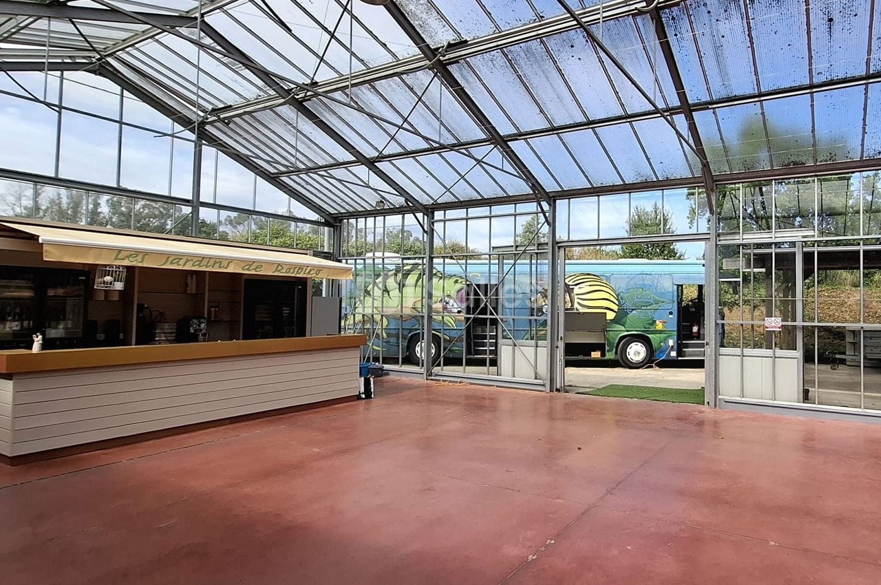 Intérieur d'une serre avec un comptoir en bois à gauche et un camion coloré visible à l'extérieur.