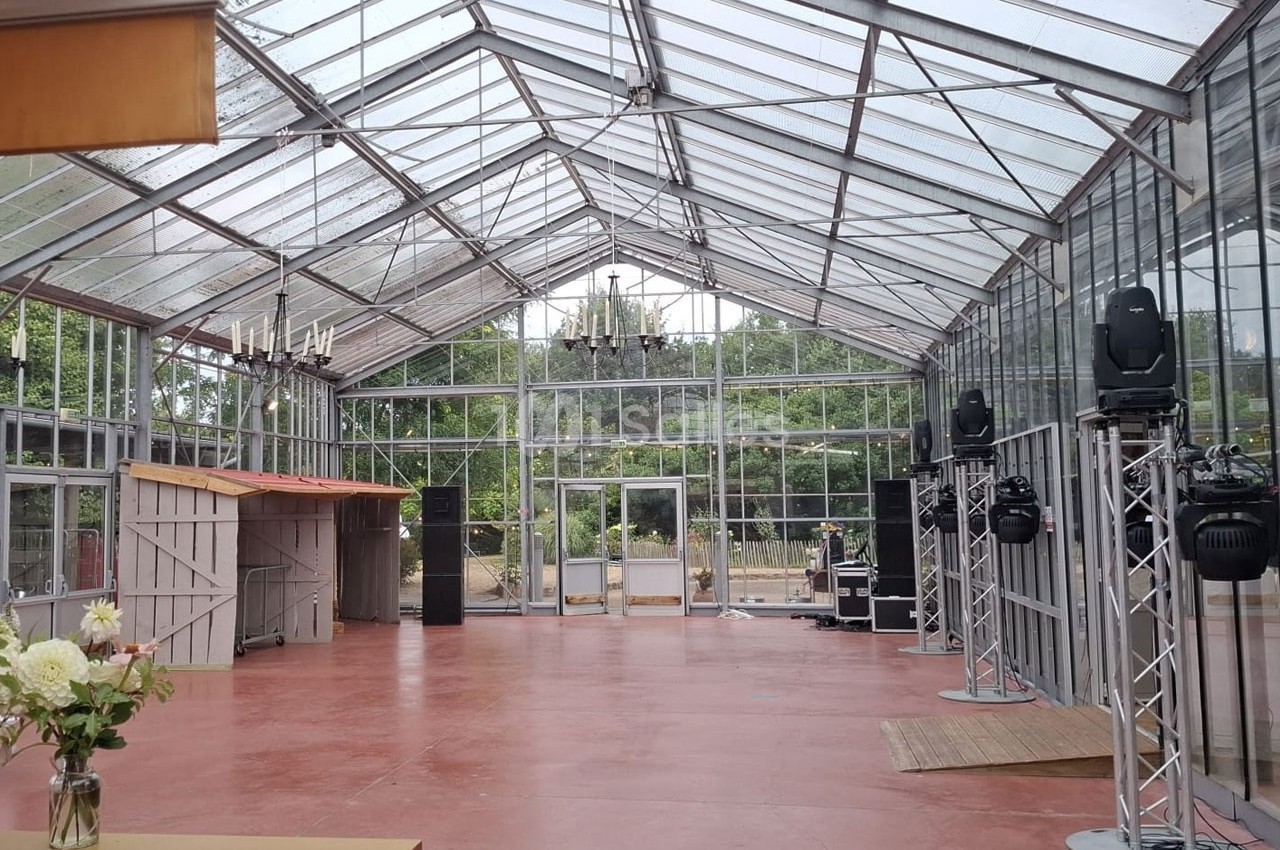 Intérieur d'une serre aménagée avec un sol rouge, des structures métalliques et des équipements d'éclairage.