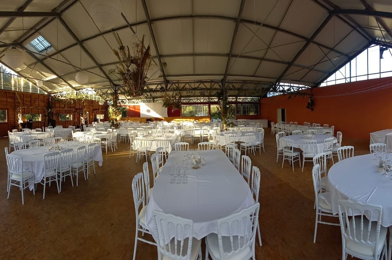 Salle de réception spacieuse avec des tables rondes dressées de nappes blanches et des chaises alignées.