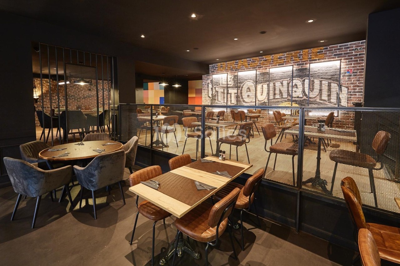 Salle de restaurant moderne avec tables en bois, chaises en cuir et mur de briques affichant une enseigne lumineuse.