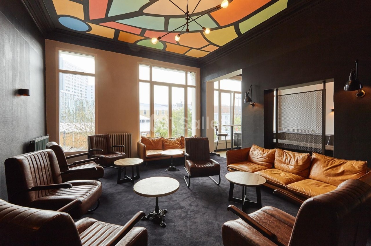 Salle de réunion avec fauteuils en cuir, tables basses, plafond coloré et grandes fenêtres laissant entrer la lumière…