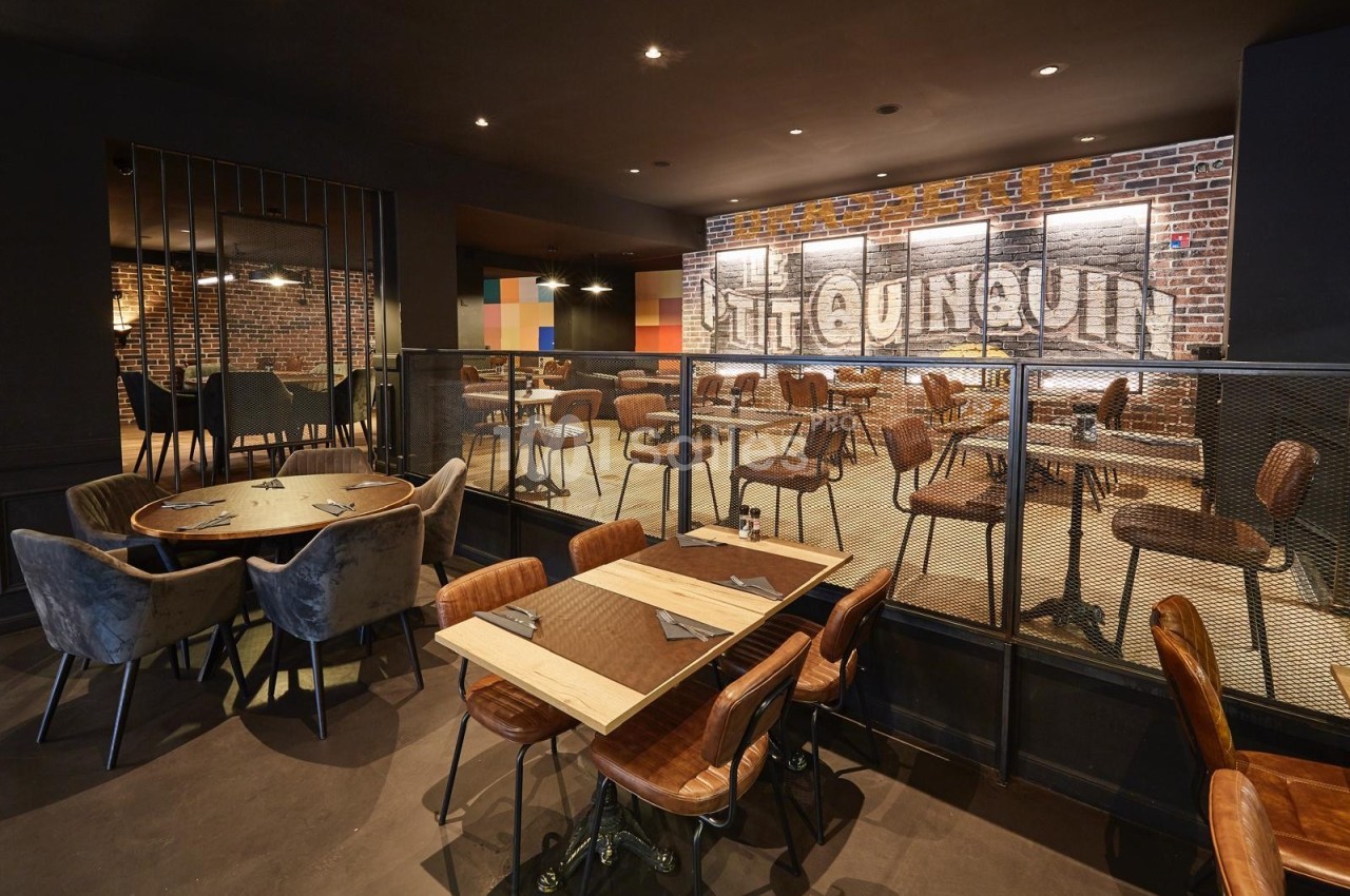 Salle de restaurant moderne avec tables en bois, chaises en cuir et mur de briques affichant une enseigne lumineuse.