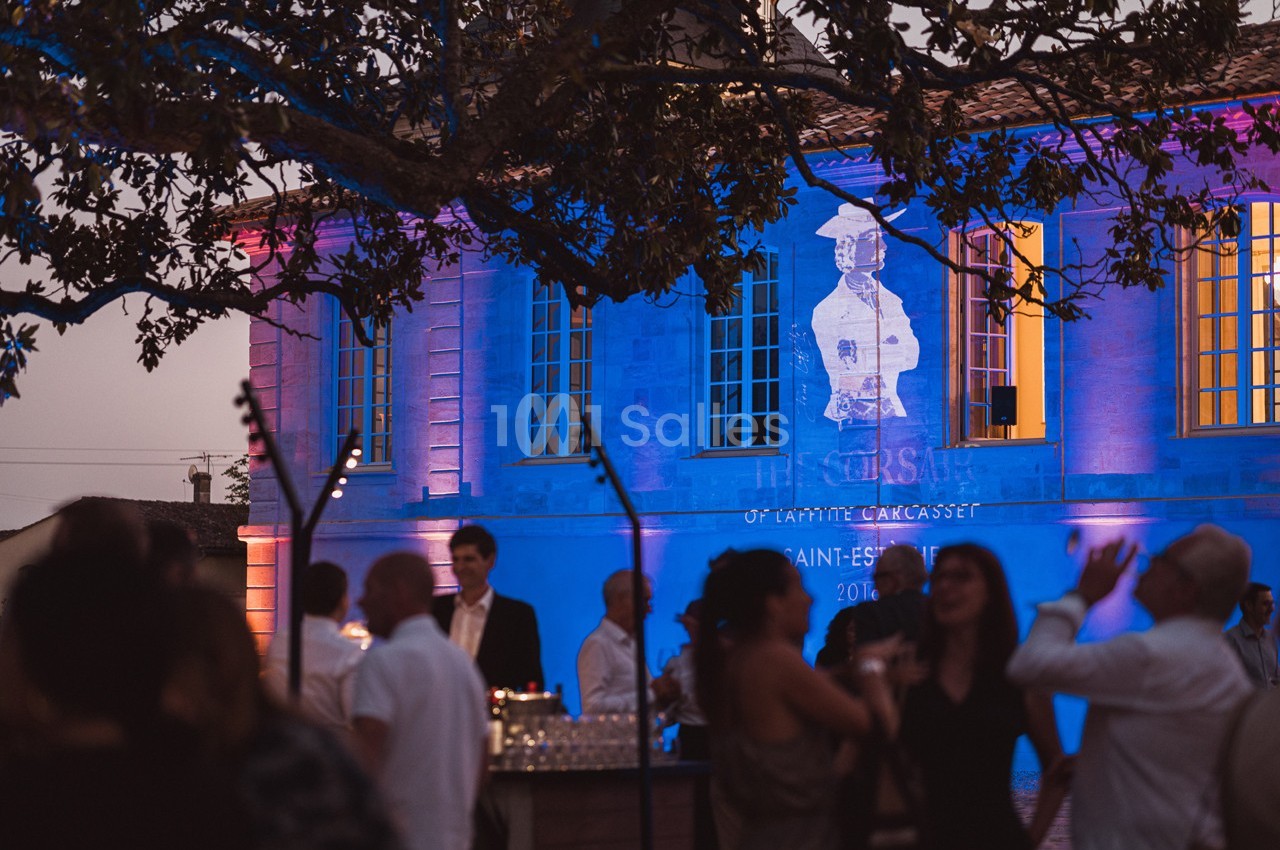 Groupe de personnes discutant en soirée devant un bâtiment illuminé avec une projection artistique sur sa façade.