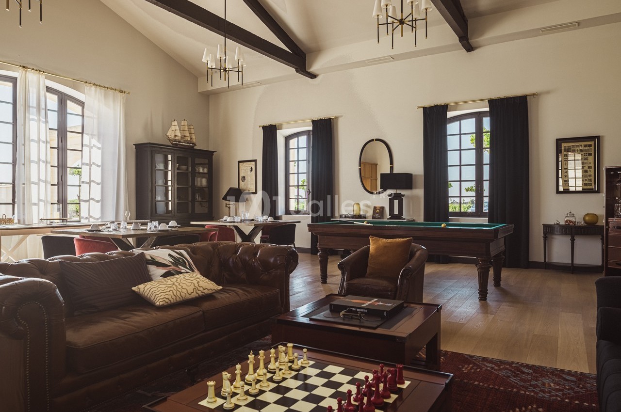 Salle élégante avec canapé en cuir, table d'échecs, billard, grandes fenêtres et décoration classique.