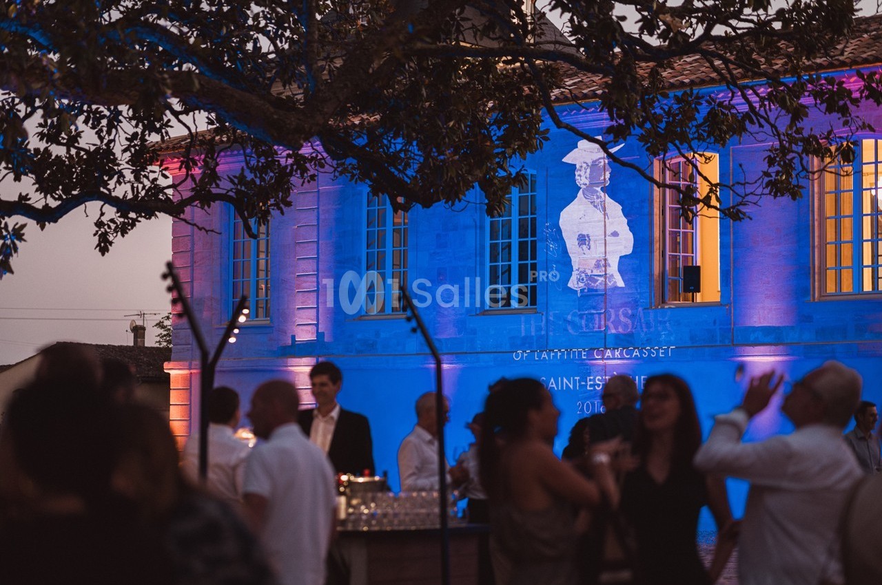 Des personnes discutent et profitent d'une soirée en plein air devant un bâtiment éclairé de lumières colorées.