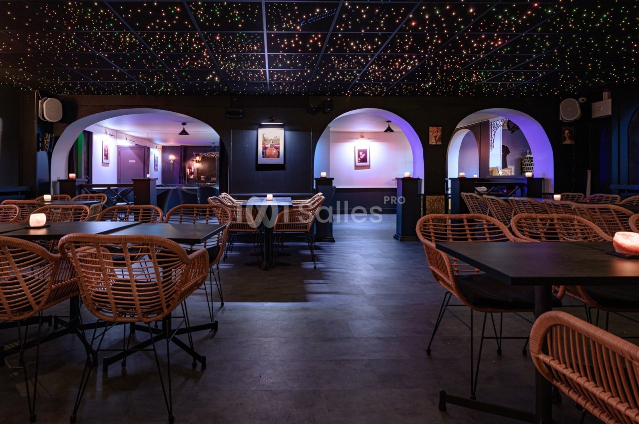 Salle avec tables et chaises en rotin, éclairage tamisé, plafond étoilé et arches décoratives.