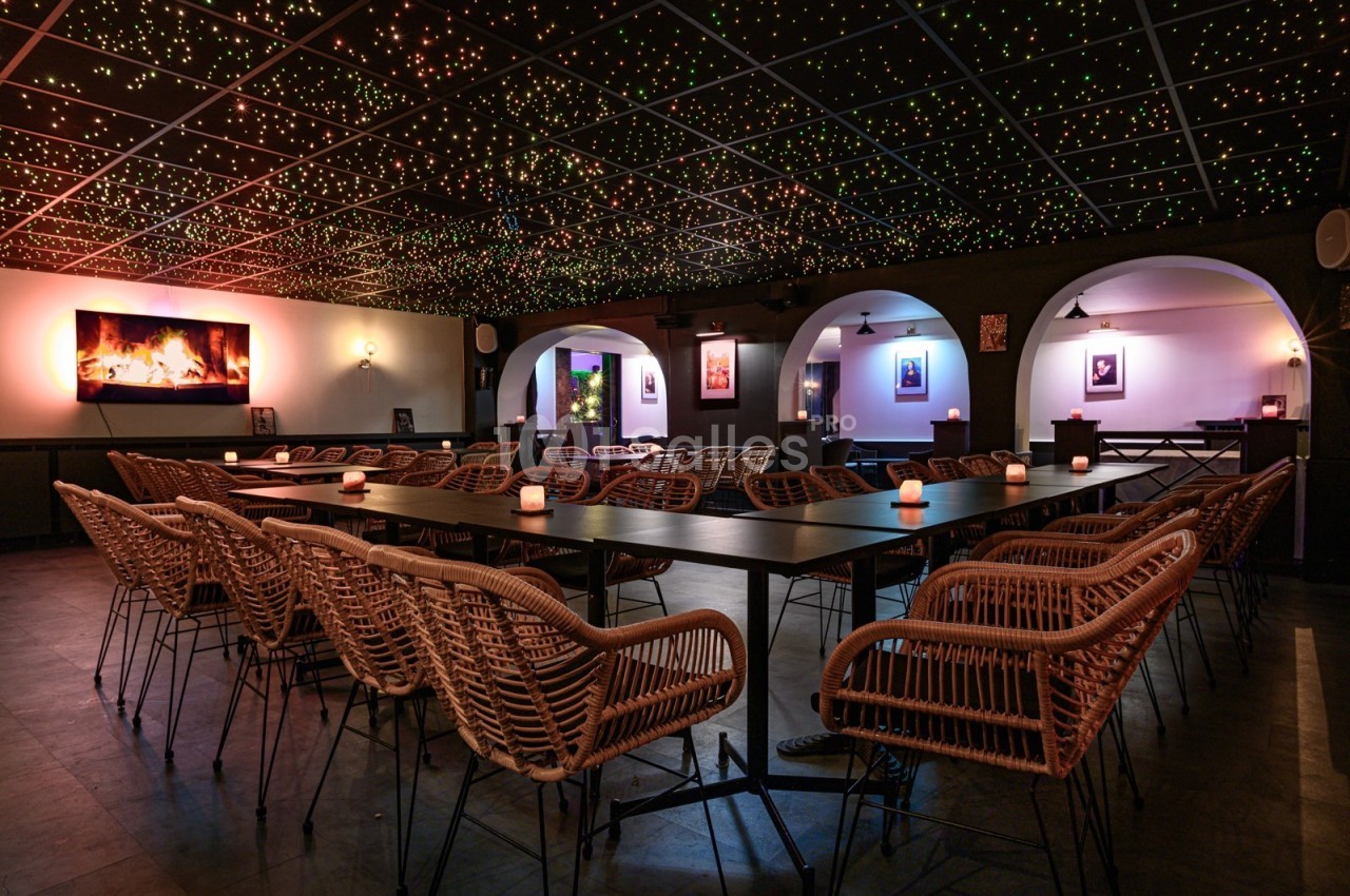 Salle de réunion avec des chaises en rotin, une grande table, un éclairage tamisé et un plafond étoilé.