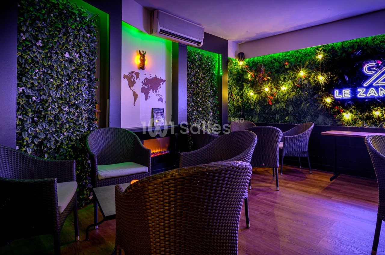 Espace lounge avec fauteuils en rotin, murs végétalisés, éclairage néon et carte du monde en décoration murale.