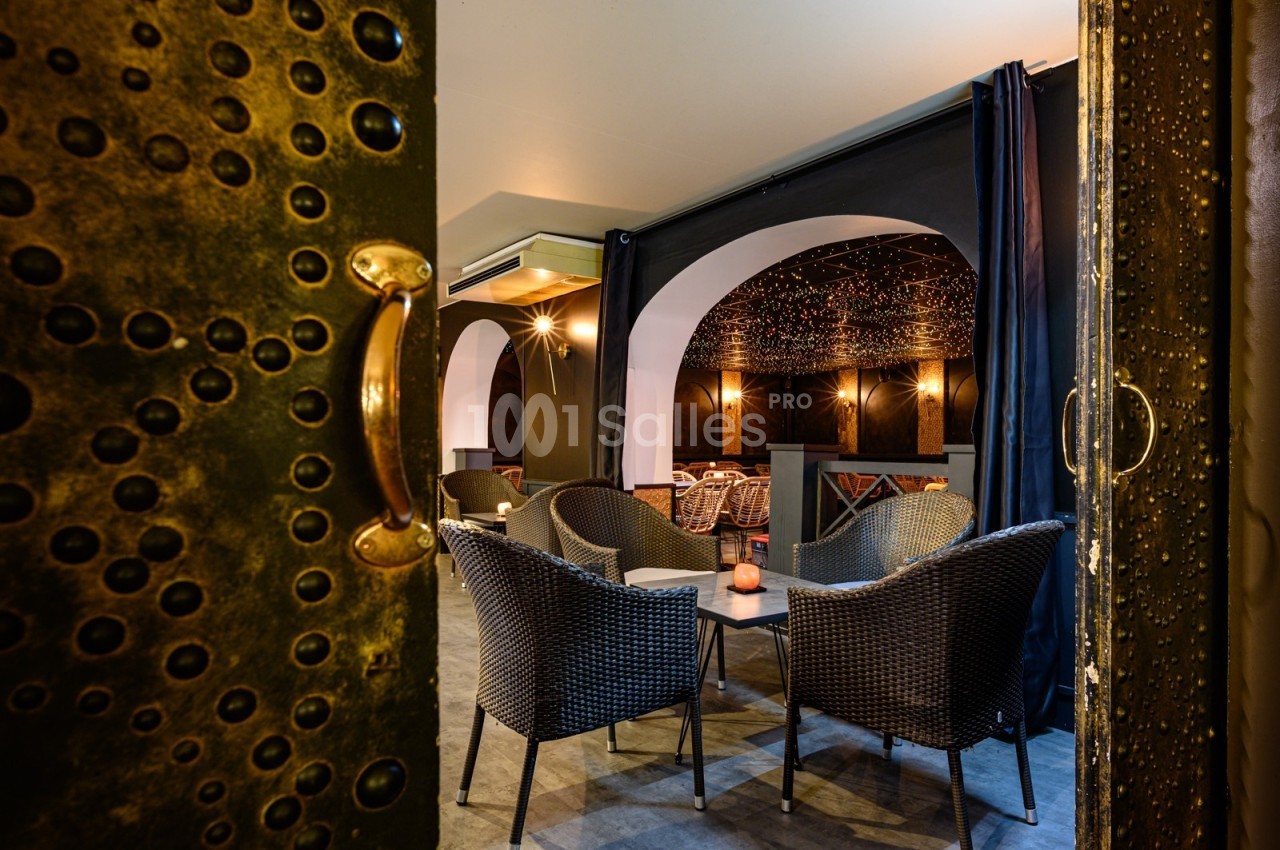 Salle avec des fauteuils en rotin, éclairage tamisé, murs sombres et plafond décoré de motifs étoilés.