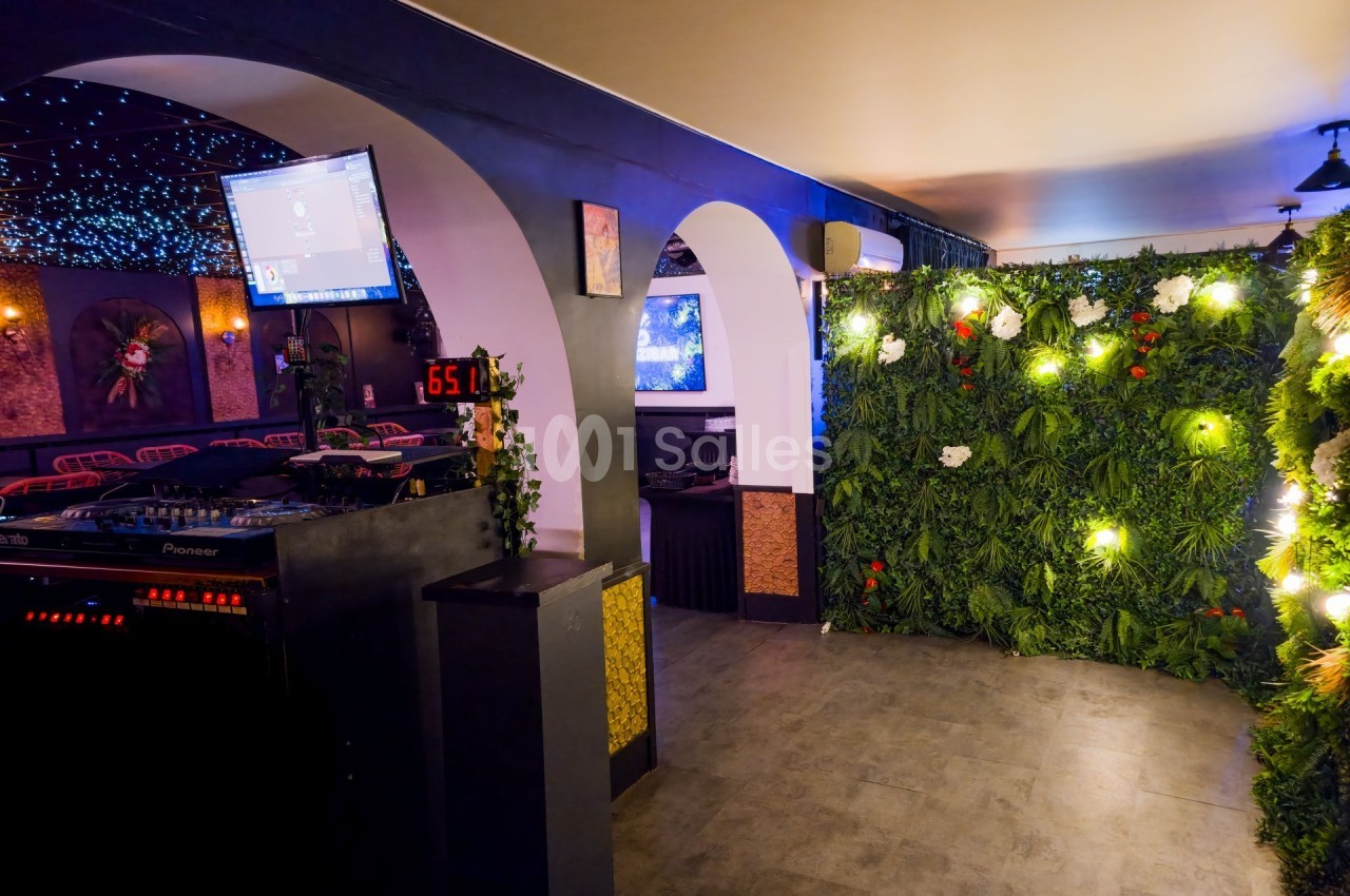 Salle décorée avec un mur végétal lumineux, des arches blanches et un espace équipé pour des événements festifs.