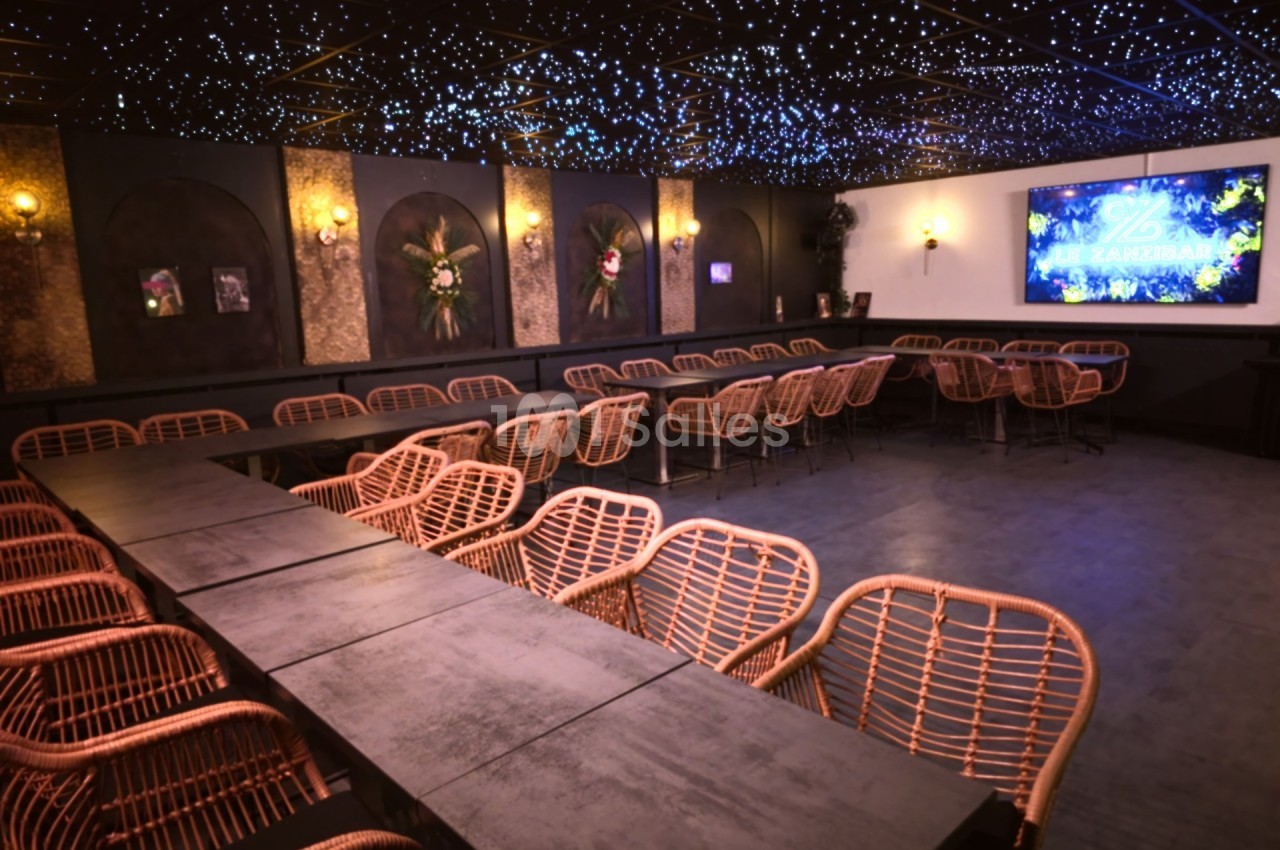 Salle de réception avec tables noires, chaises en rotin, éclairage étoilé au plafond et écran mural lumineux.