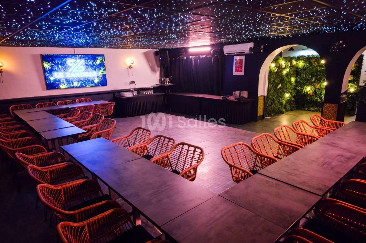 Salle de réunion avec tables disposées en U, chaises en rotin, éclairage tamisé et mur végétal en arrière-plan.