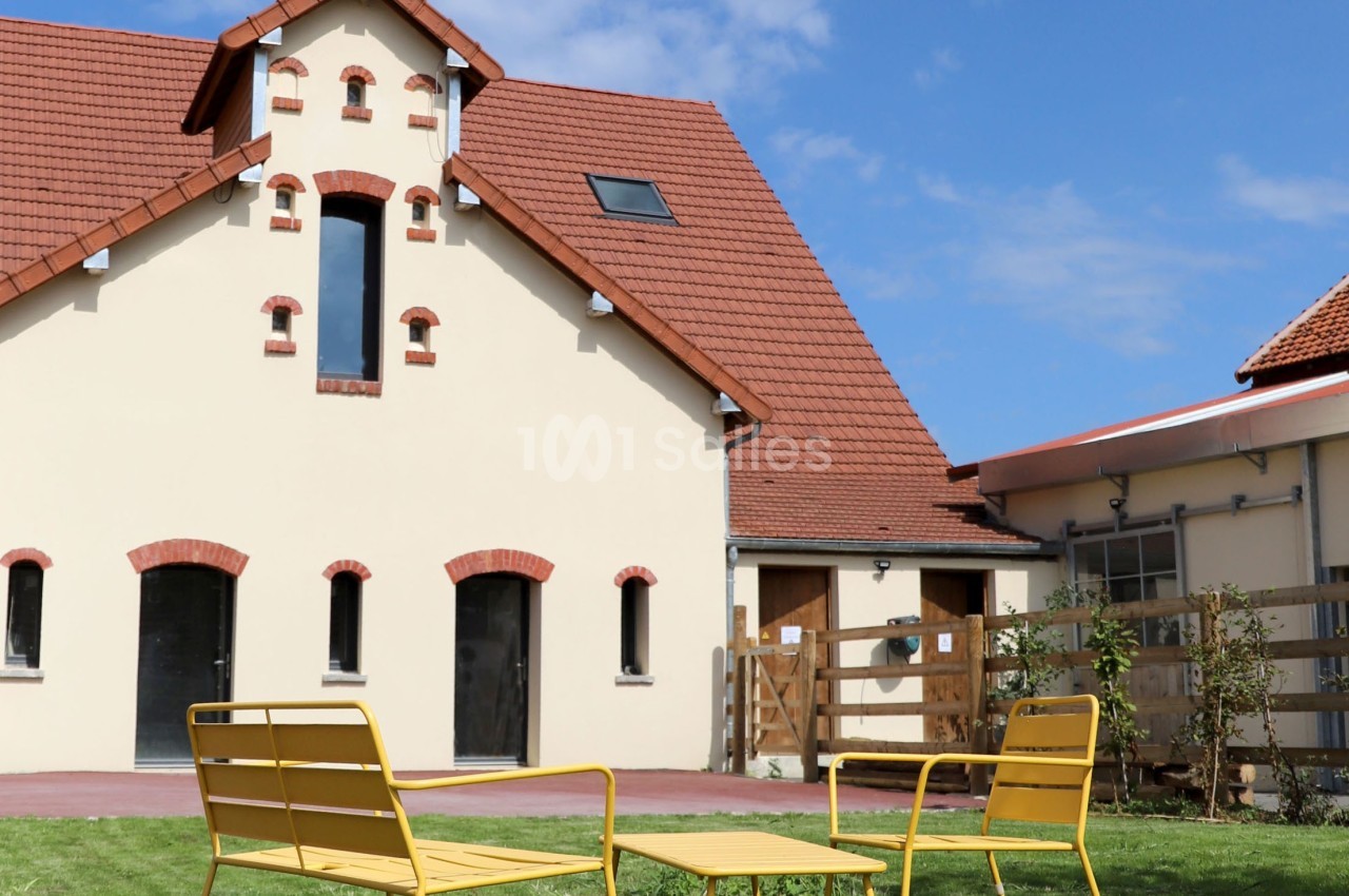 Façade d'une maison avec toit en tuiles rouges, jardin aménagé et mobilier de jardin jaune sur pelouse.