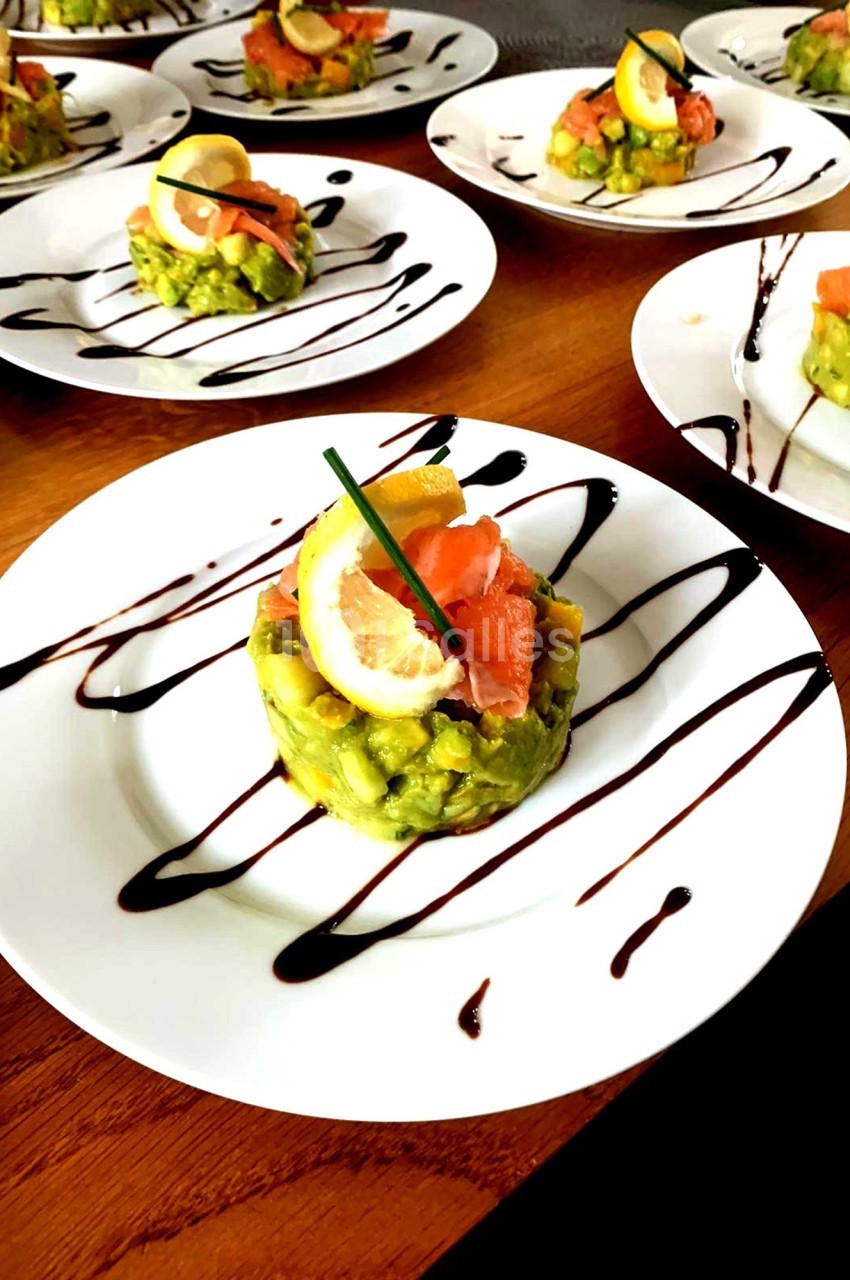 Assiette contenant un tartare d'avocat et saumon fumé, décoré de citron, ciboulette et filet de sauce balsamique.