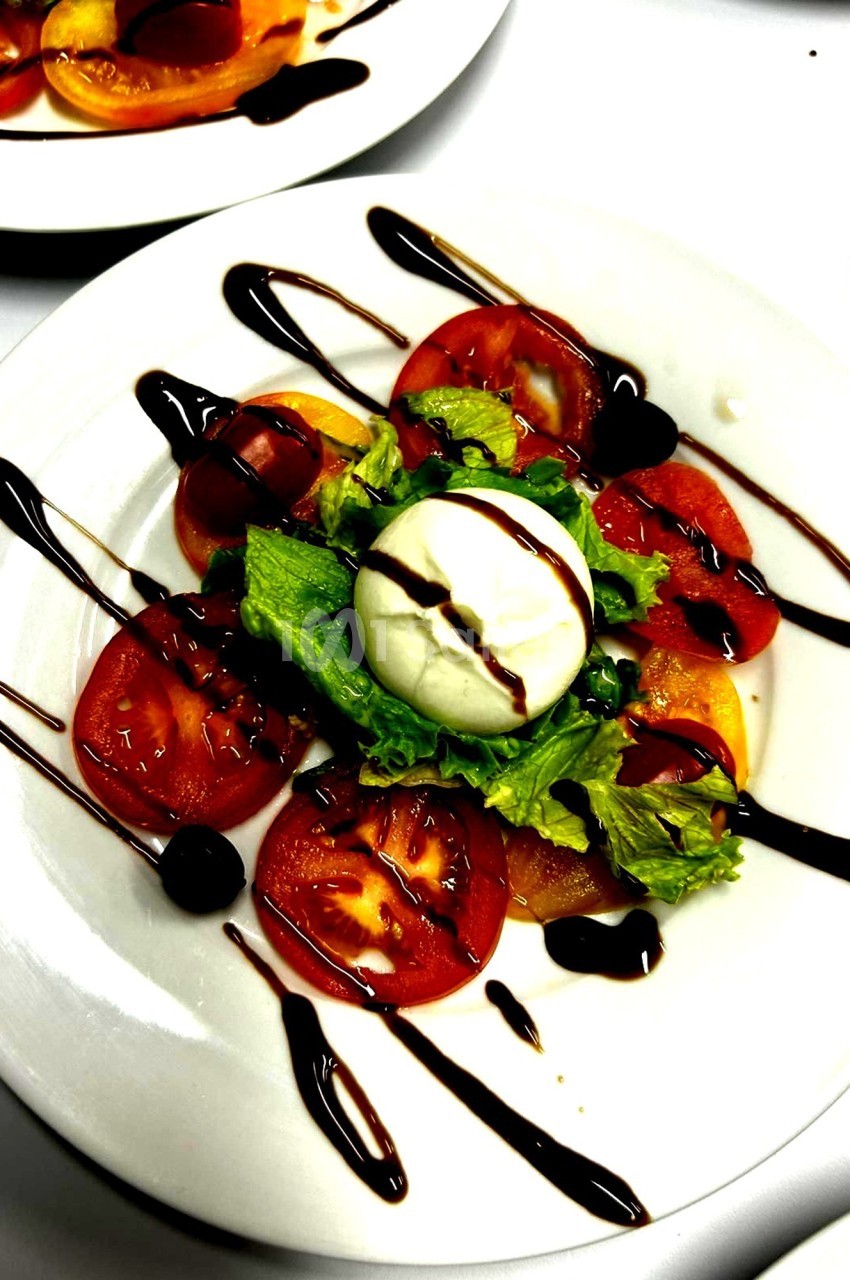 Assiette de salade composée de tomates, mozzarella, laitue et filet de vinaigre balsamique.