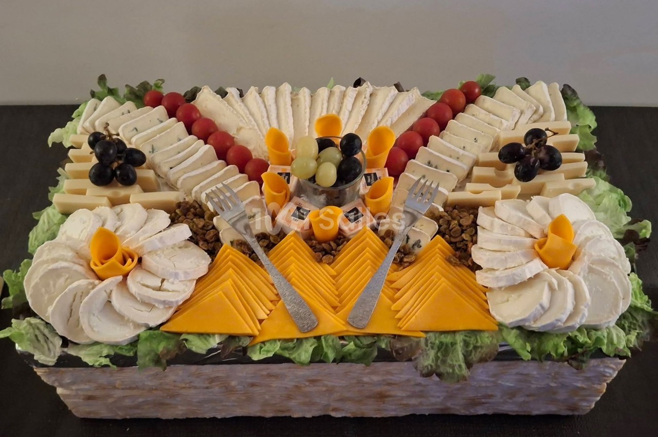 Plateau de fromages variés joliment disposés avec raisins, tomates cerises et décorations sur un lit de salade verte.