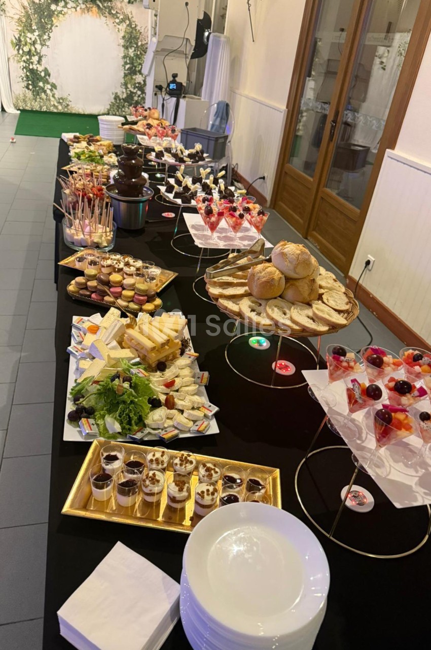 Buffet varié avec desserts, fromages, pains et fontaine de chocolat, disposé sur une longue table noire.