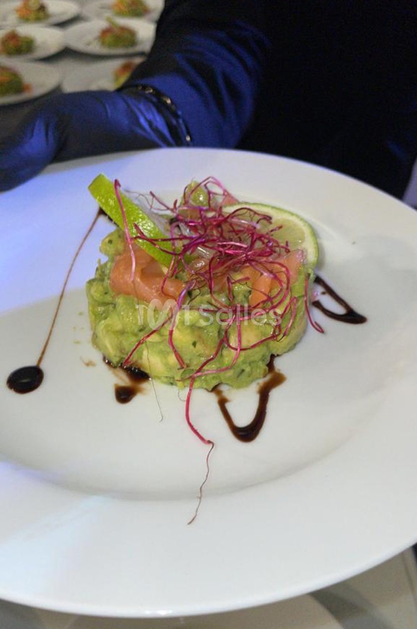 Assiette de tartare d'avocat garni de saumon fumé, citron vert, pousses rouges et filet de sauce balsamique.
