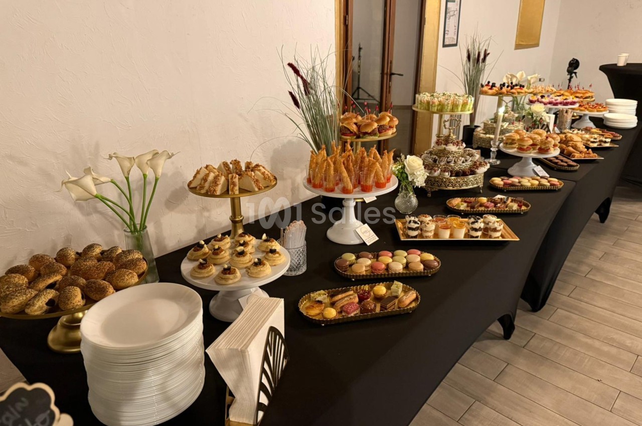 Buffet varié avec pâtisseries, viennoiseries, macarons et décorations florales sur une table noire.