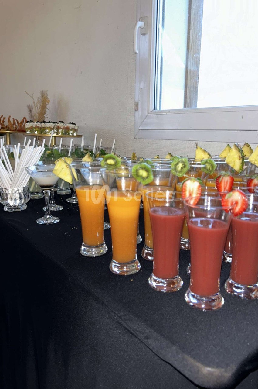Verres de jus colorés garnis de fruits frais alignés sur une table noire près d'une fenêtre.