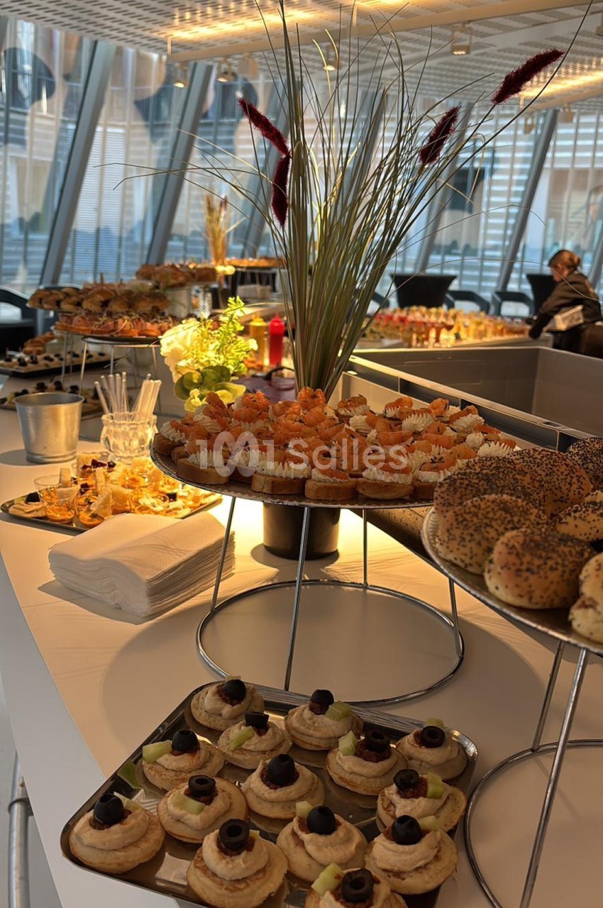Buffet avec assortiments de viennoiseries, canapés, bagels et décorations végétales dans un espace lumineux.
