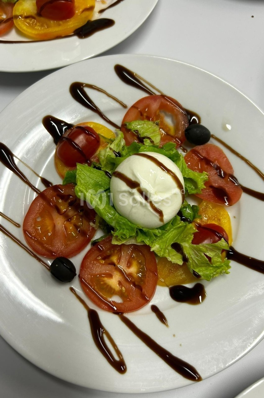 Assiette de salade composée avec tomates, mozzarella, laitue, olives noires et filet de vinaigre balsamique.