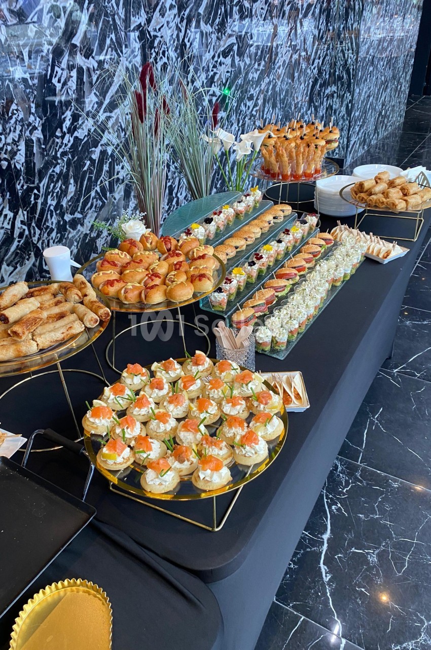 Buffet avec une variété de bouchées salées, incluant canapés, roulés et mini-sandwichs, sur une table noire.