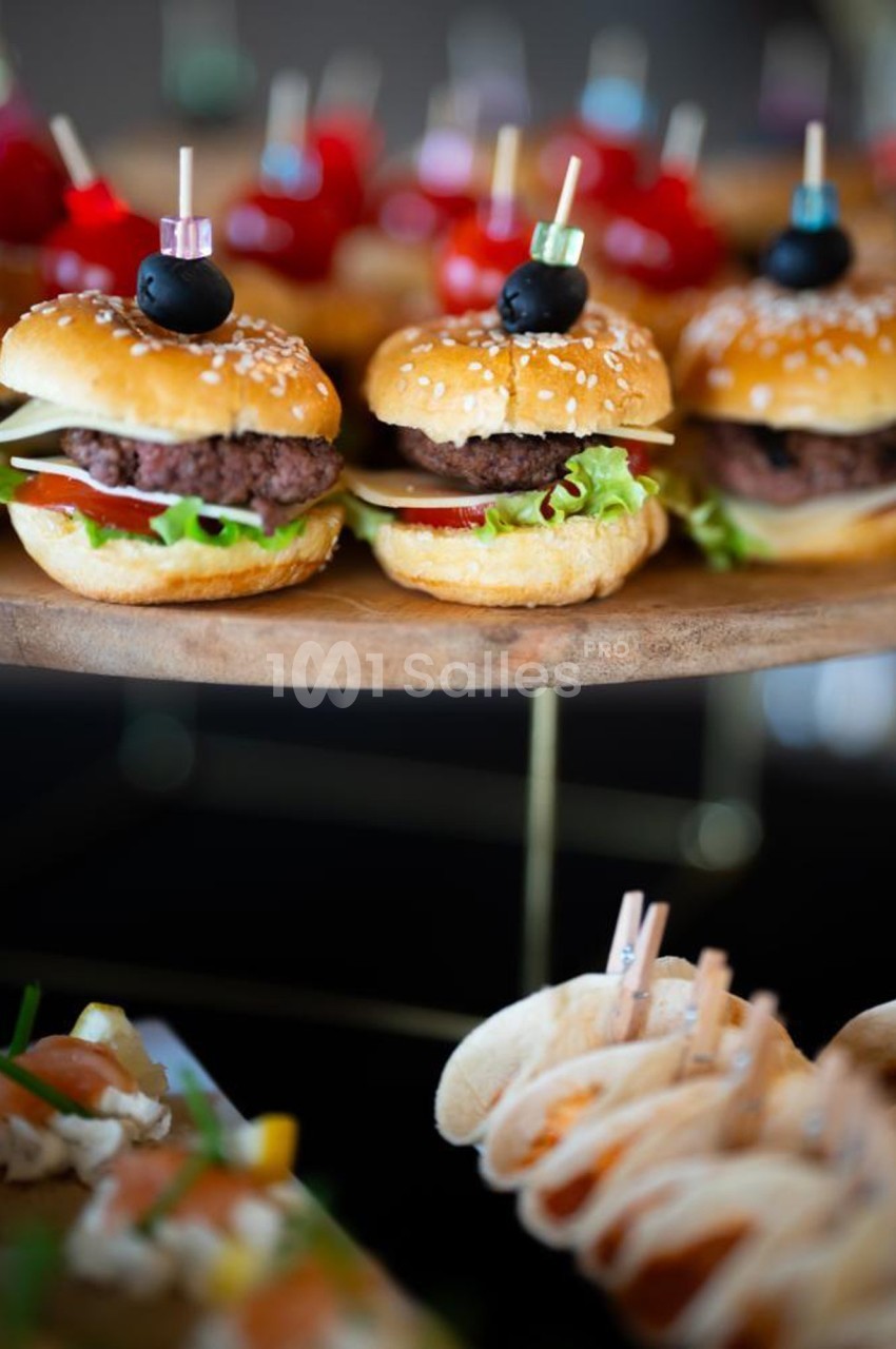 Mini burgers garnis de salade, tomate et steak, présentés sur un plateau en bois avec d'autres amuse-bouches.