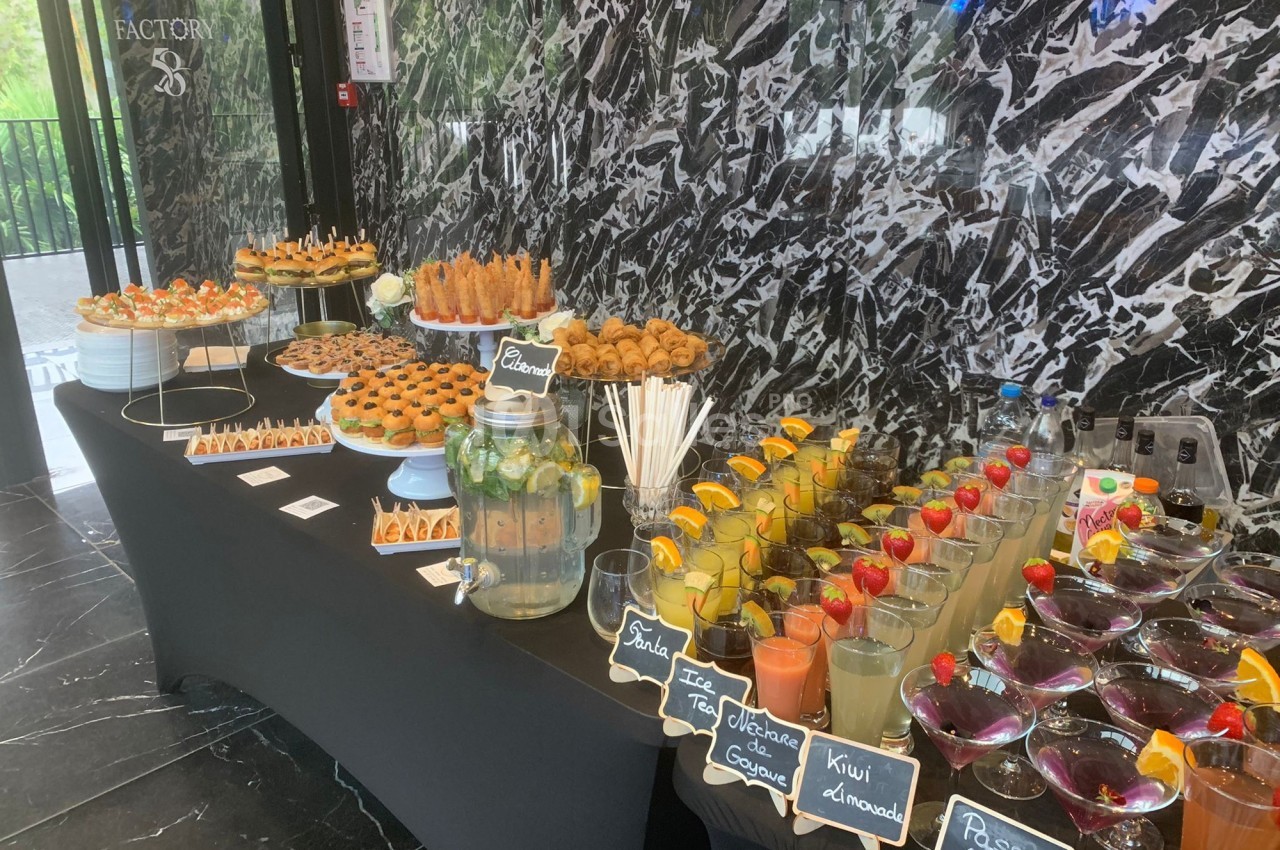 Buffet avec boissons fruitées, verrines, pâtisseries et snacks salés disposés sur une table noire devant un mur marbré.
