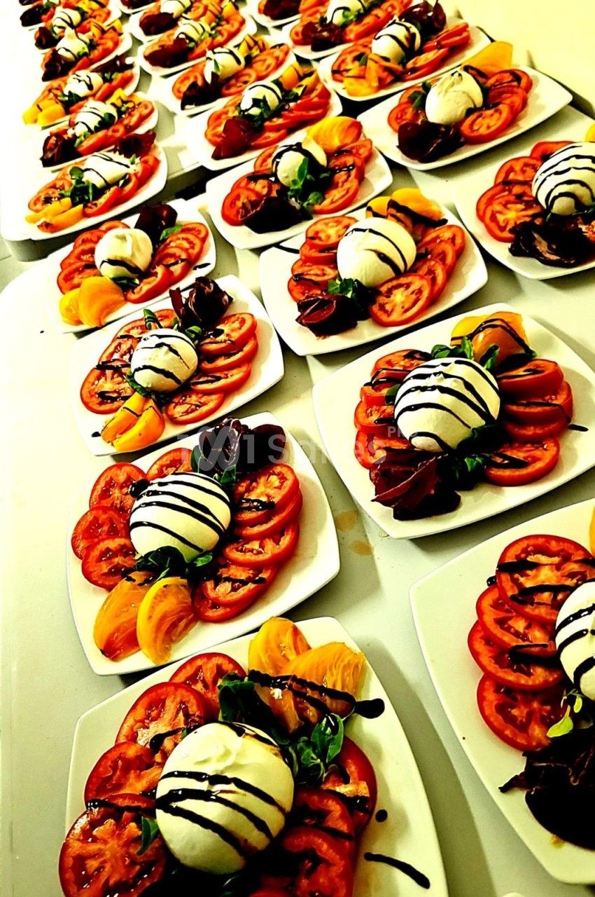 Assiettes alignées de salades caprese avec tomates, mozzarella, basilic et filet de vinaigre balsamique.