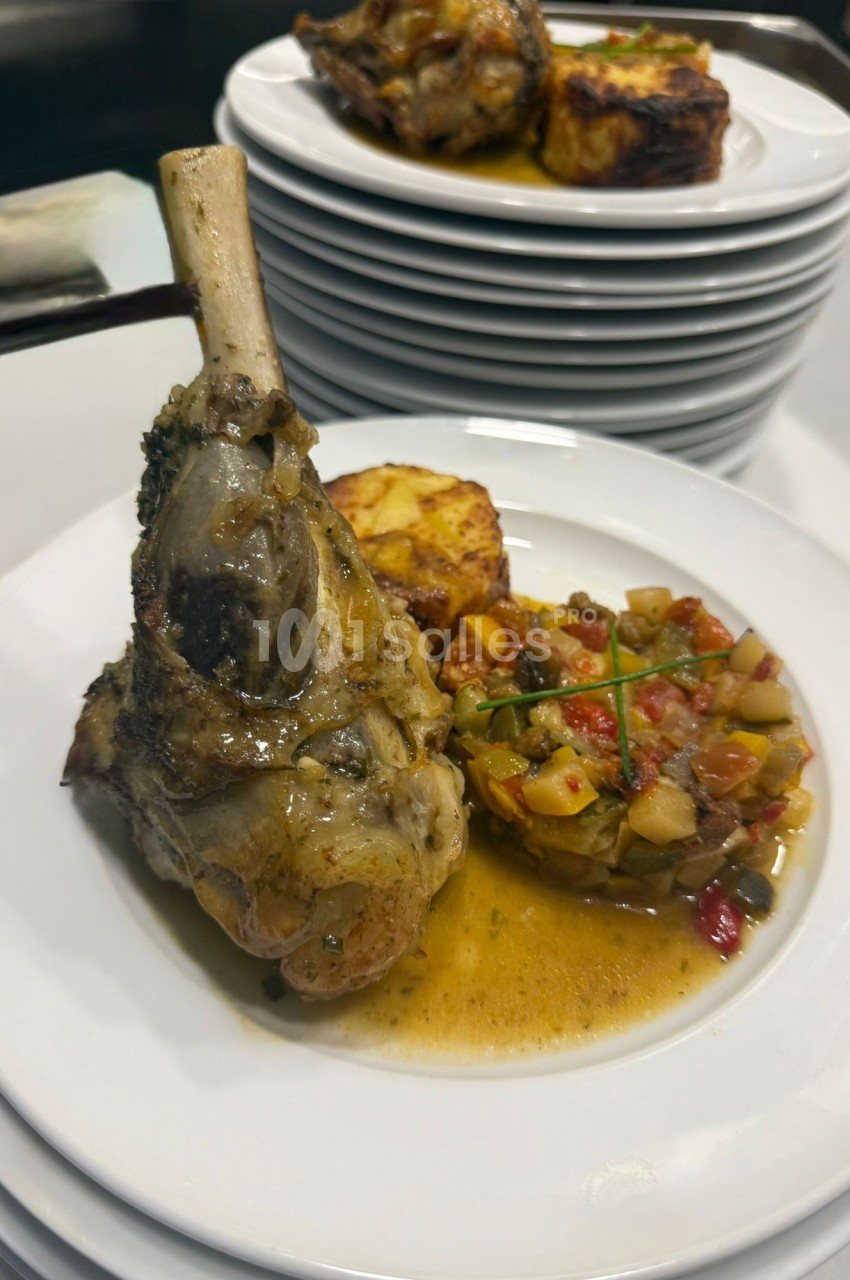 Assiette contenant un jarret d'agneau en sauce, accompagné de légumes mijotés et d'un gratin de pommes de terre.
