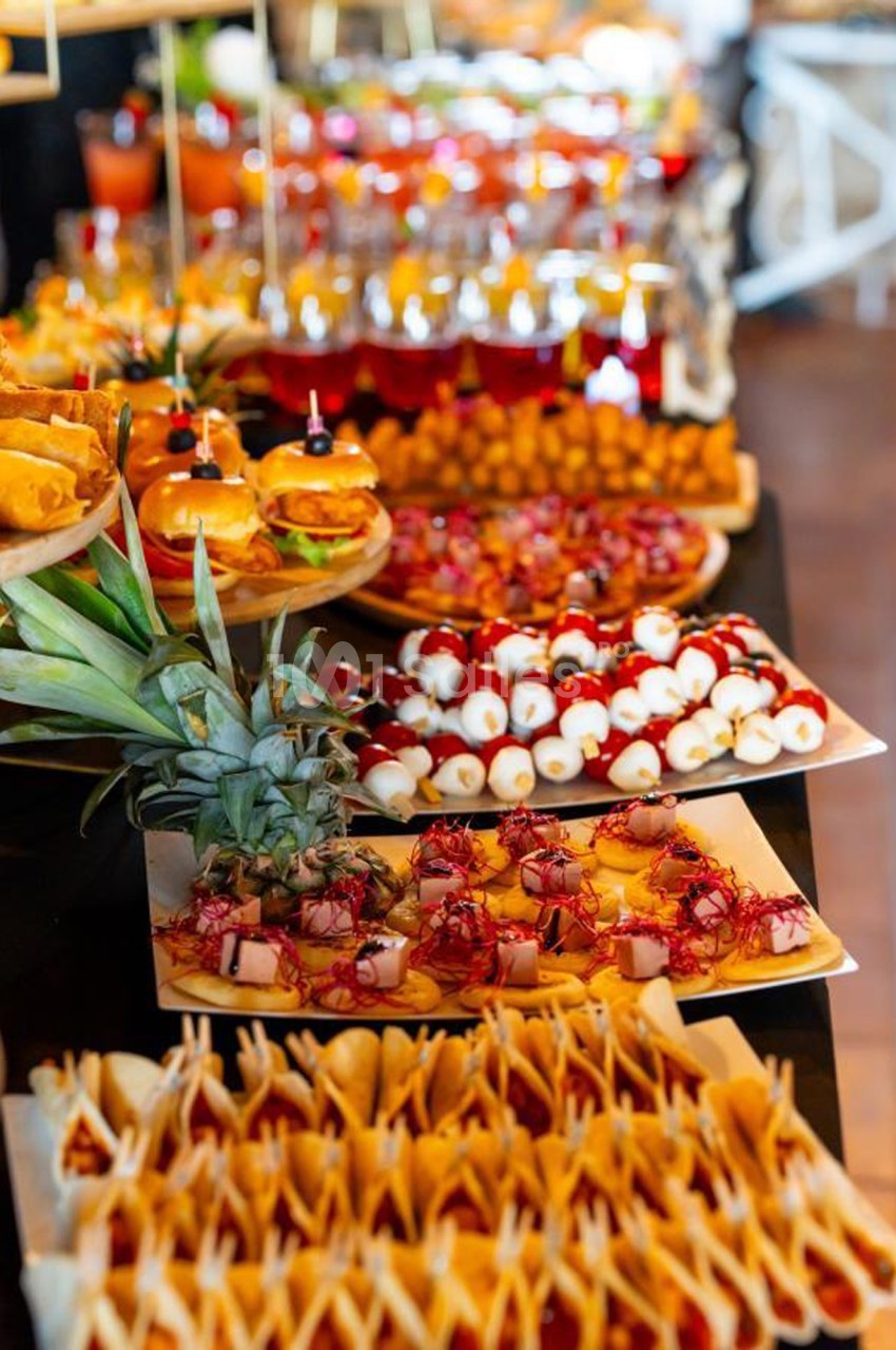 Buffet coloré avec divers plats, dont brochettes, mini-burgers, fruits et amuse-bouches disposés sur une table.
