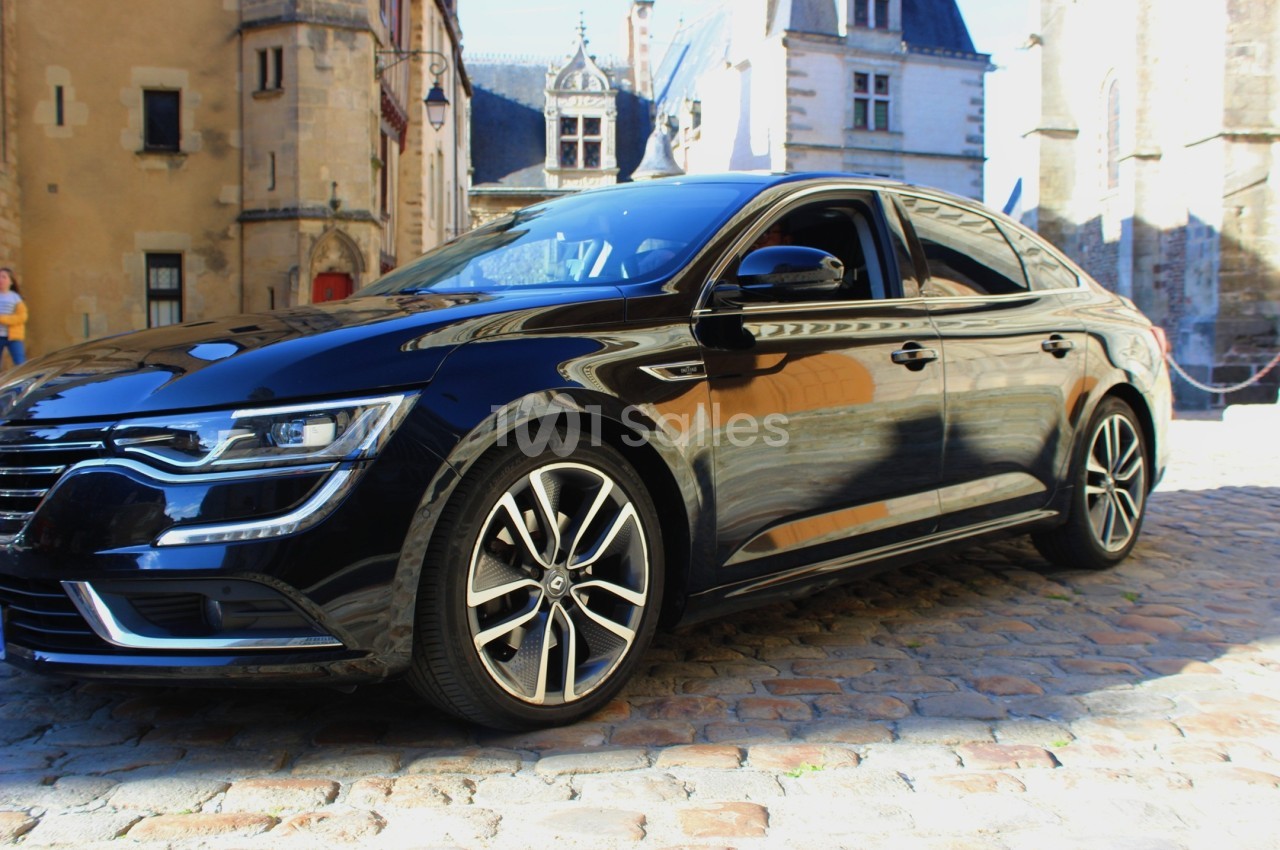 Voiture noire garée sur des pavés devant des bâtiments historiques en arrière-plan.