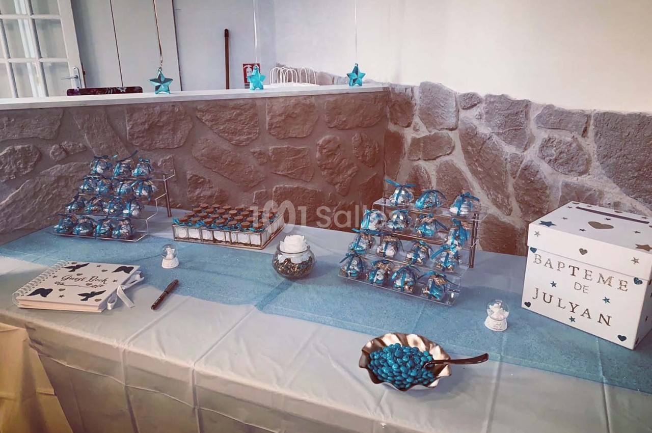 Table décorée pour un baptême avec des friandises bleues, une urne blanche et des éléments de décoration étoilés.