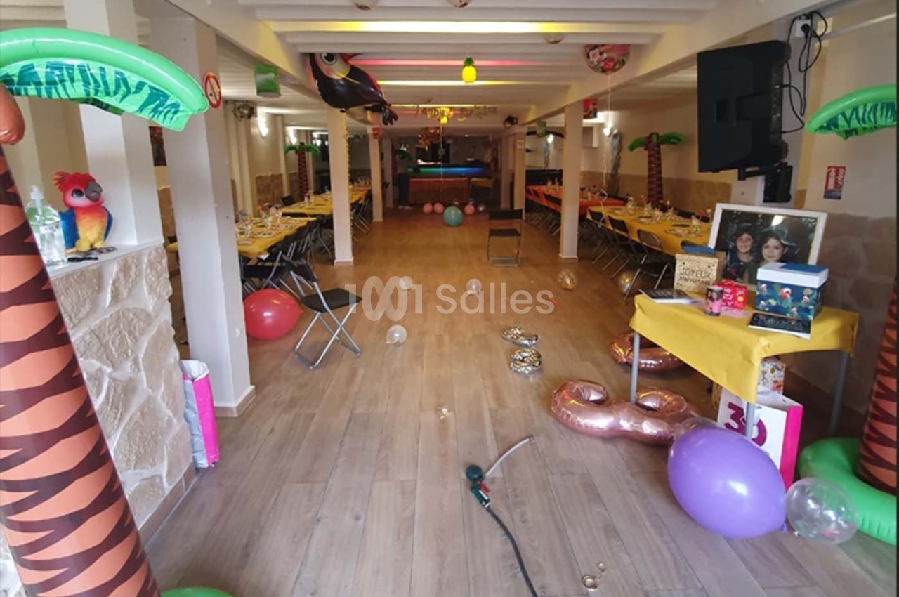Salle décorée sur le thème tropical avec tables dressées, ballons colorés et palmiers gonflables.
