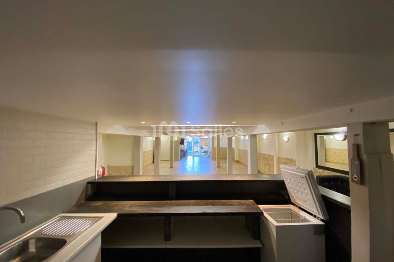 Vue d'un espace intérieur avec un comptoir, un évier, un congélateur ouvert et un couloir éclairé en arrière-plan.
