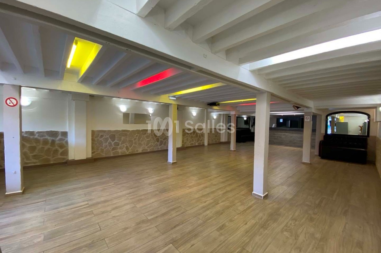 Salle vide avec sol en parquet, murs en pierre et plafond blanc avec éclairage coloré intégré.