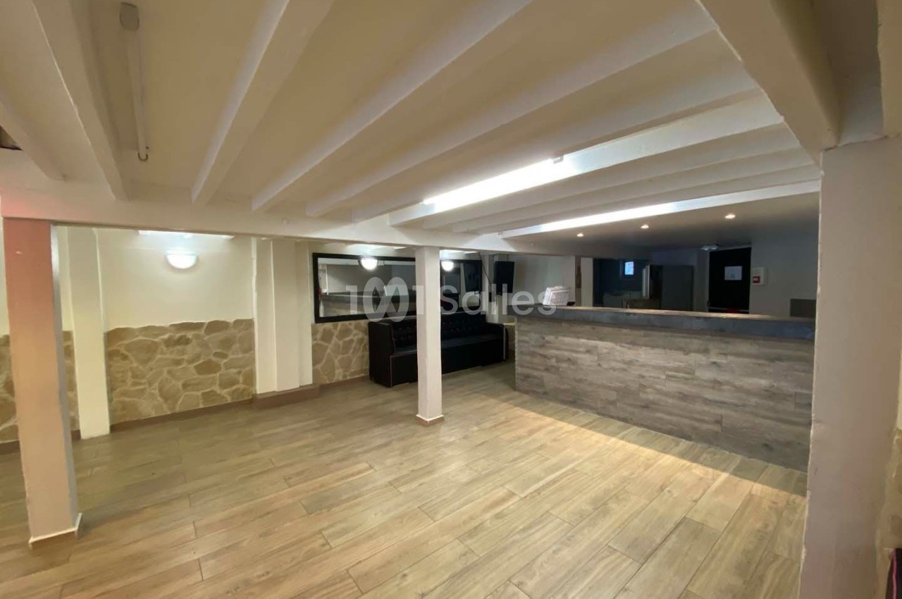 Salle vide avec sol en parquet, murs en pierre et crépi, poutres apparentes au plafond, et comptoir en bois.