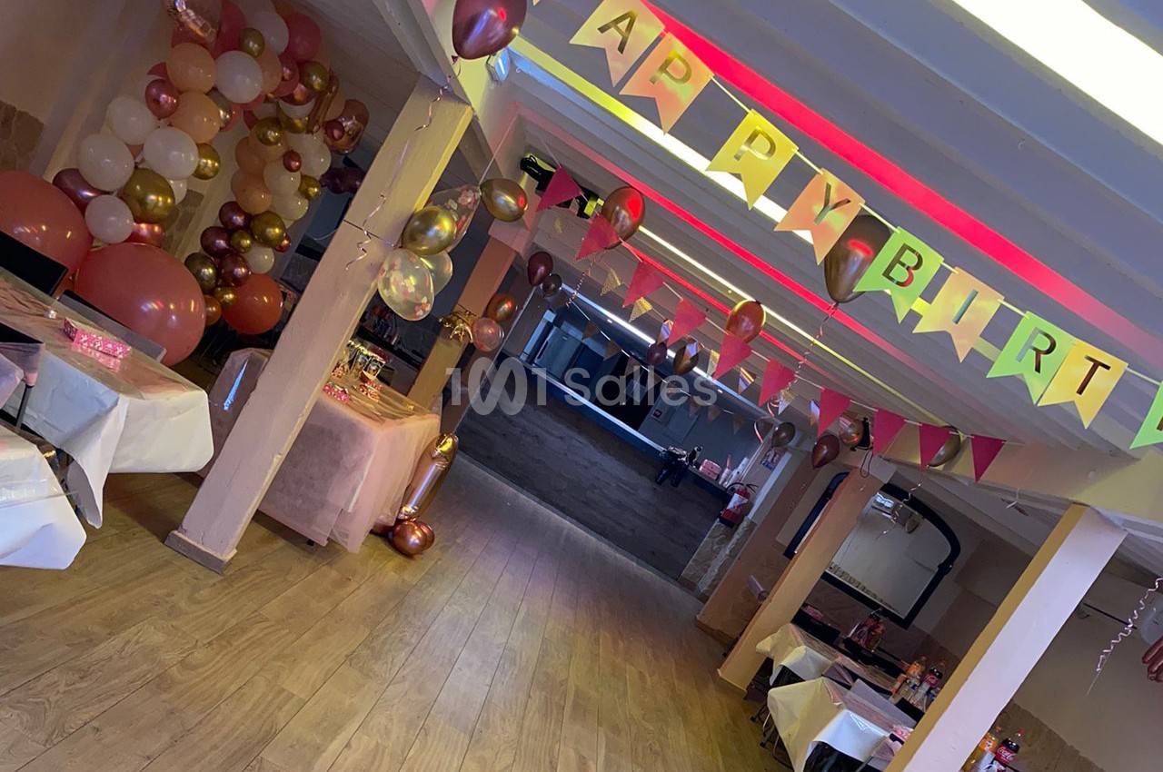 Salle décorée pour un anniversaire avec des ballons, des guirlandes colorées et des tables dressées.