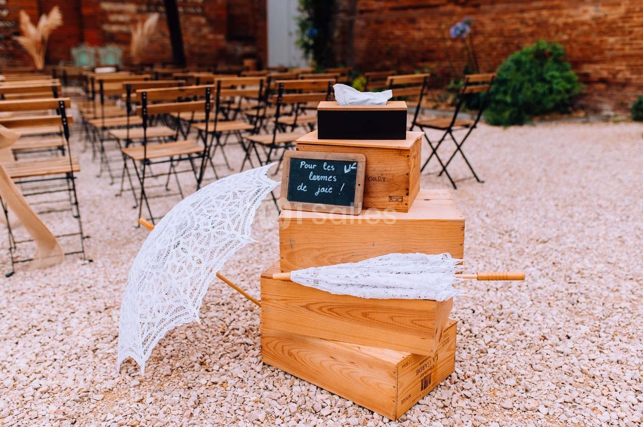 Boîtes en bois empilées avec un parapluie blanc en dentelle et une ardoise indiquant ’Pour tes larmes de joie’.