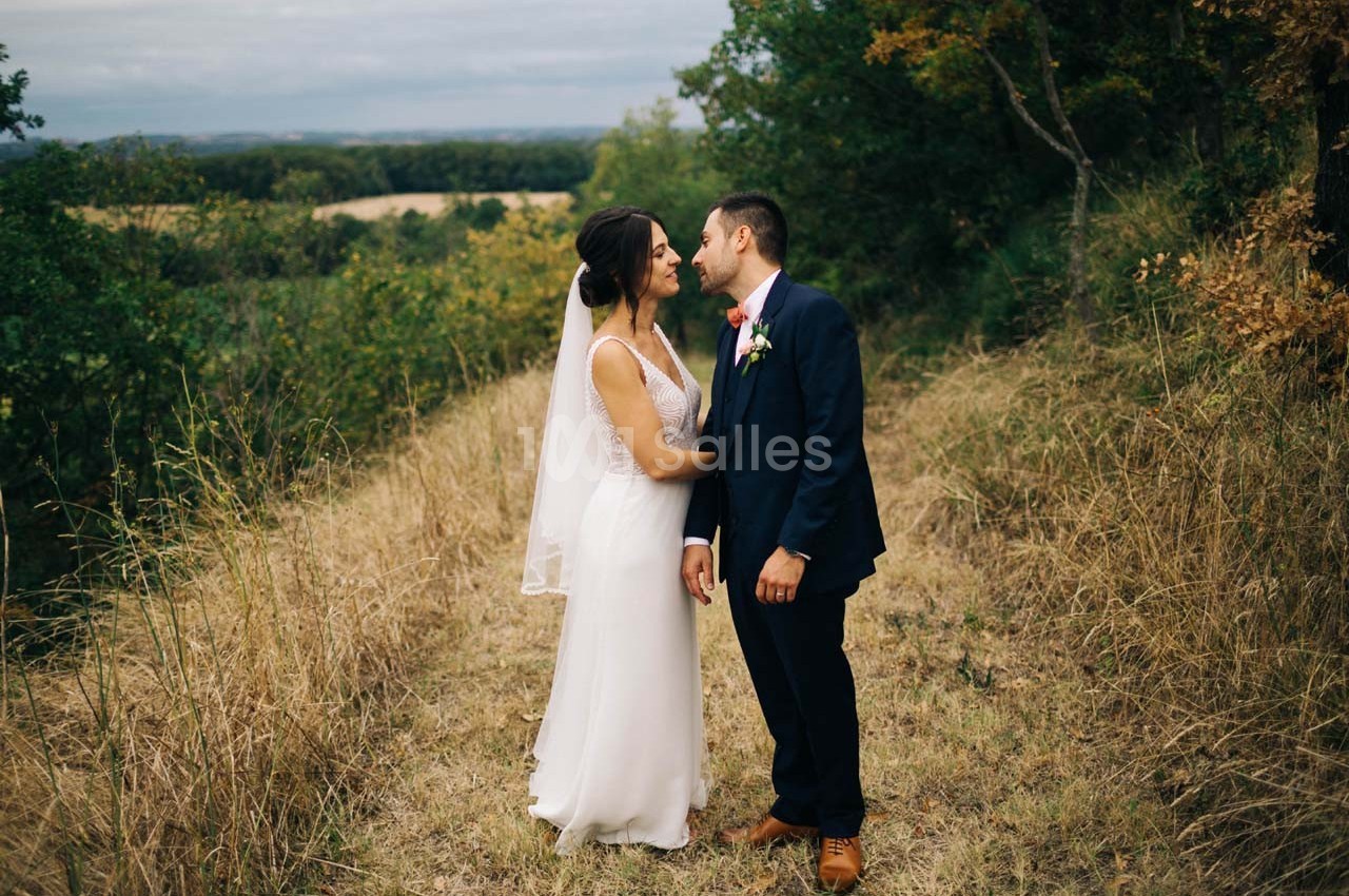 Un couple en tenue de mariage se tient sur un chemin herbeux entouré de végétation, échangeant un moment intime.