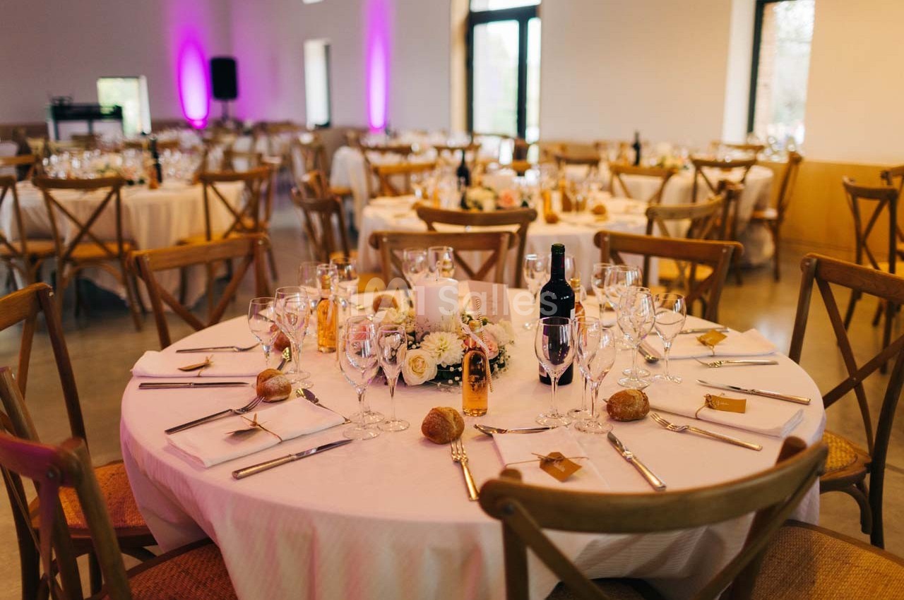 Salle de réception avec tables rondes dressées, décorées de fleurs, bougies et couverts élégants.