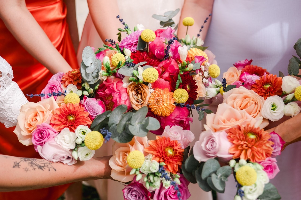 Quatre bouquets de fleurs colorés avec des roses, des dahlias et des feuillages, tenus par des personnes en tenue élégante.
