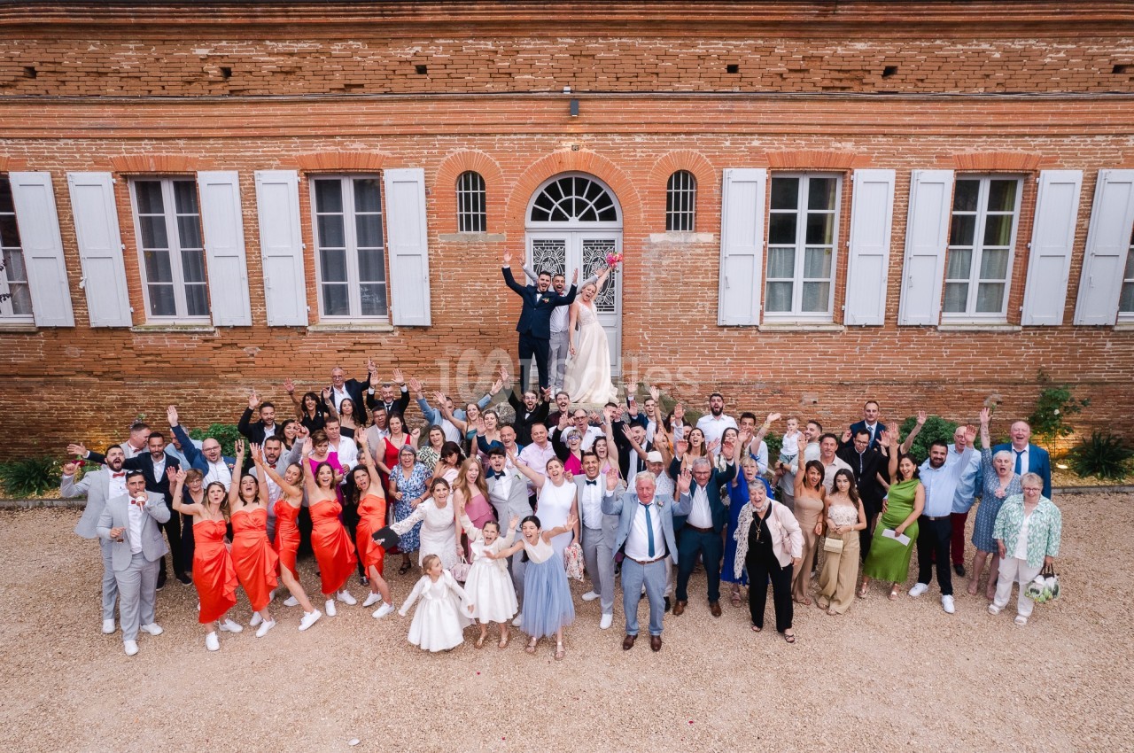 Groupe de personnes rassemblées devant un bâtiment en briques, célébrant un mariage avec des tenues festives.