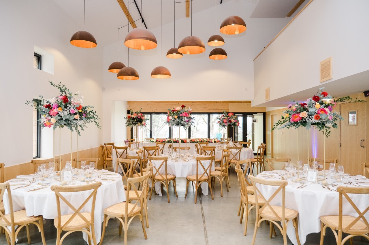 Salle de réception lumineuse avec tables rondes décorées de fleurs colorées et suspensions en cuivre au plafond.