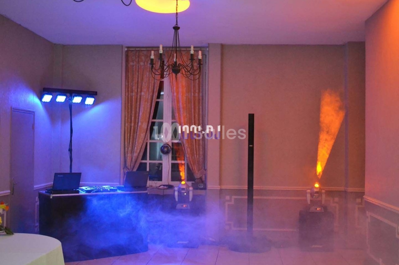 Salle équipée pour un événement avec jeux de lumière, table de mixage et fumée diffusée au sol.