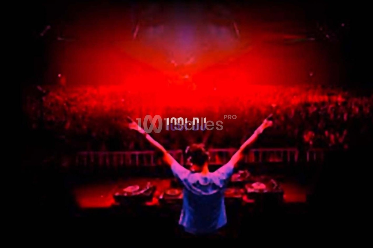 Un DJ de dos, bras levés, face à une foule dans une ambiance lumineuse rouge.